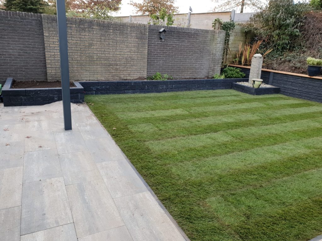 Grijs gemeleerde sierbestrating met graszoden en plantenbak van antraciet linea's