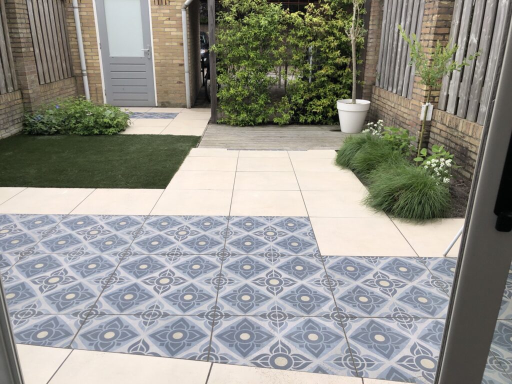 Terras met effen en gedessineerde keramische tegels naast kunstgras